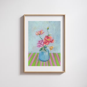 May include: A framed pastel painting of a blue vase holding colourful flowers. The flowers are pink, red, and yellow. The vase sits on a table with green and pink stripes. The background is a light blue.