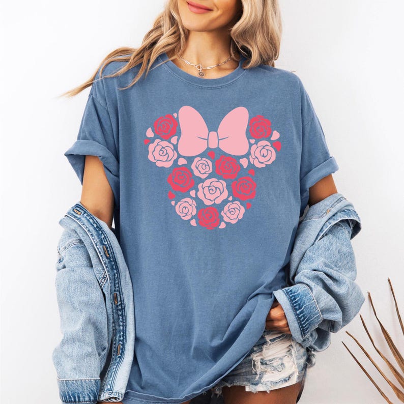 May include: A blue t-shirt with a pink floral design in the shape of a bow. The design is made up of pink and red roses.
