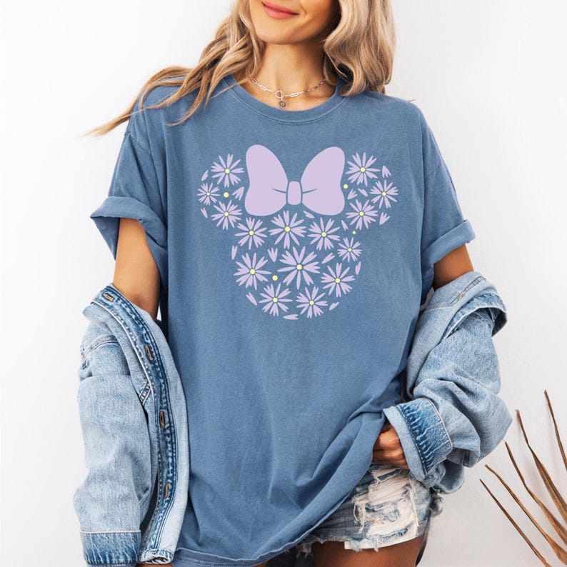 May include: A blue t-shirt with a purple flower design in the shape of a mouse head with a bow.