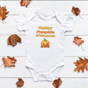 Op de afbeelding: Witte baby romper met de tekst "Cutest Pumpkin of the patch" in oranje en gele letters. Onder de tekst staat een cartoon-pompoen met een glimlach.