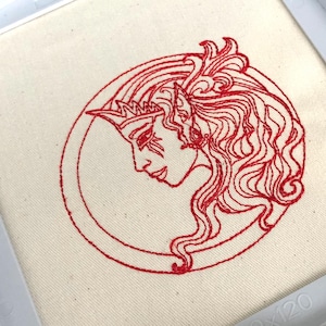 May include: Red embroidered design of a woman's face with long hair, wearing a crown, inside a circle on a white fabric.