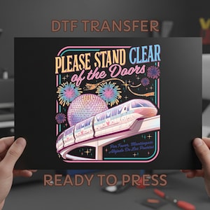 May include: Black graphic featuring a monorail, fireworks, and a geodesic sphere. Text reads "PLEASE STAND CLEAR of the Doors" and "READY TO PRESS". The design has a retro, colorful style.