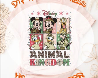 Może przedstawiać: Biała koszulka z kolorowym wzorem przedstawiającym Myszki Miki, Minnie, Donalda i Goofy ubranych w stroje safari. Wzór zawiera tekst "Disney" i "Animal Kingdom" z wzorem lamparta. Koszulka jest gotowa do prasowania za pomocą transferu termicznego.