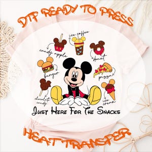 May include: A light pink t-shirt featuring a graphic of Mickey Mouse surrounded by various snacks including a candy apple, ice coffee, donut, burger, pizza, chocolate candy, and ice cream. The text reads "Just Here For The Snacks".