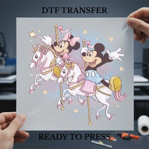 May include: DTF TRANSFER image featuring Mickey and Minnie Mouse riding carousel horses. The image has a light blue background with stars and the text "READY TO PRESS". The characters are in a cartoon style with pink and yellow accents.