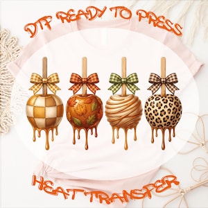 May include: A light pink t-shirt featuring a DTF READY TO PRESS HEAT TRANSFER graphic of four caramel apples on sticks. The apples have different patterns: plaid, autumn leaves, drizzled caramel, and leopard print, each topped with a bow.