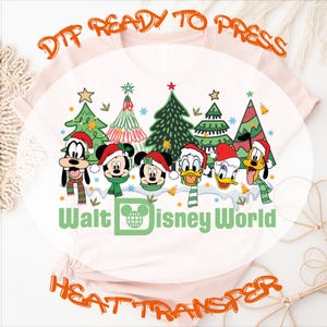 DTF ready-to-press heat transfer featuring a Christmas-themed design.  The design showcases Goofy, Mickey Mouse, Minnie Mouse, Donald Duck, and Daisy Duck in Santa hats, positioned in front of stylized Christmas trees.  The text 'Walt Disney World' is prominently displayed below the characters. The design is on a light pink shirt.  This is a digital design for heat transfer onto apparel.