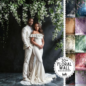 Könnte beinhalten: Ein Paar posiert vor einem schwarzen Hintergrund mit herabhängenden weißen Blumen. Die Frau trägt ein weißes, schulterfreies Kleid und der Mann einen weißen Anzug. Der Text "30+ FLORAL WALL BACKDROP loft." befindet sich in der unteren rechten Ecke des Bildes.