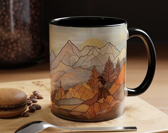May include: A black ceramic mug featuring a colourful illustration of a mountain landscape with trees and a sun rising over the peaks. The mug has a black handle.