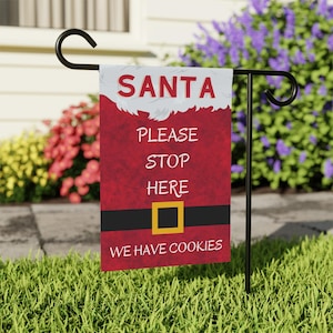 May include: A red and white Christmas garden flag with a Santa Claus design. The flag reads "Santa Please Stop Here We Have Cookies".