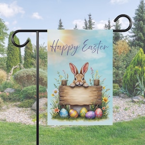 May include: A Happy Easter garden flag with a brown bunny rabbit peeking over a wooden sign with colorful Easter eggs at the base. The flag has a blue sky background with white clouds and a sun shining in the top right corner.