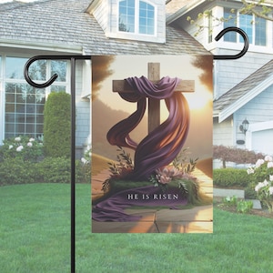 May include: A purple cloth draped over a wooden cross with the text "He is Risen" at the base. The cross is set against a background of a sunrise with a blurred landscape.