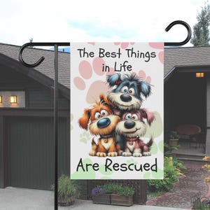 May include: A garden flag featuring three cartoon dogs stacked together. The flag has the text "The Best Things in Life Are Rescued" with paw prints in the background. The dogs are brown, blue, and pink.