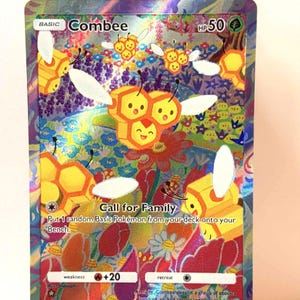 May include: A holographic Combee Pokémon trading card. The card features a yellow and orange honeycomb design with Combee characters, flowers, and the text "Call for Family". The card is displayed on a wooden easel.