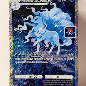 Könnte beinhalten: Eine holografische Alolan Ninetales Pokémon-Karte. Die Karte zeigt ein blaues fuchsartiges Wesen mit neun Schwänzen, mit dem Text "Alolan Ninetales" und "Blizzard". Die Karte hat 110 KP und eine Schwäche von +20.