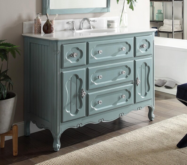 Puede incluir: Un mueble de ba&ntilde;o azul claro con encimera blanca y lavabo integrado. El mueble tiene varios cajones y puertas con pomos de cristal. La moldura decorativa y las patas curvas completan el dise&ntilde;o. Un espejo est&aacute; montado encima.