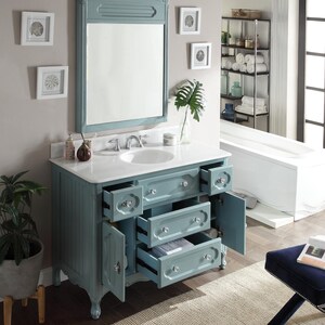 Puede incluir: Un mueble de ba&ntilde;o azul claro con encimera blanca y espejo enmarcado a juego. El mueble tiene m&uacute;ltiples cajones y puertas de armario con pomos de cristal. El ba&ntilde;o cuenta con un lavabo blanco y obras de arte enmarcadas.