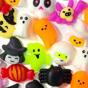 May include: A collection of small, colorful Halloween-themed resin cabochons featuring various shapes including ghosts, skulls, pumpkins, bats, spiders, eyeballs, candy, and haunted houses in vibrant shades of orange, black, white, green, and purple.