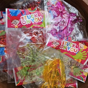May include: Multiple clear plastic bags containing colorful, translucent, sticky toys in various shapes including a spider web and abstract forms. Each bag features a header card with the text STUCK ON YOU and a cartoon character illustration.