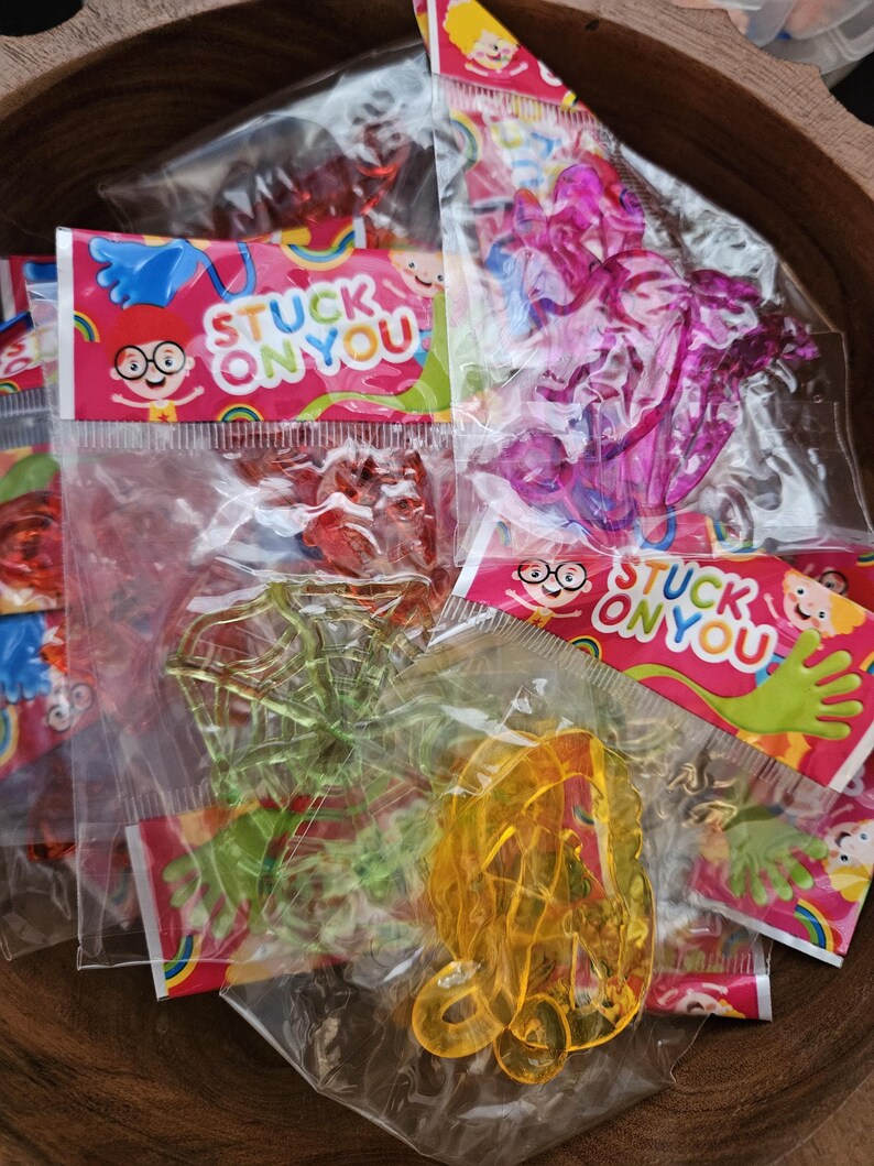 May include: Multiple clear plastic bags containing colorful, translucent, sticky toys in various shapes including a spider web and abstract forms. Each bag features a header card with the text STUCK ON YOU and a cartoon character illustration.