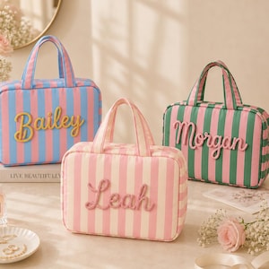 Könnte beinhalten: Drei rechteckige, gestreifte Kulturtaschen mit Tragegriffen. Eine Tasche ist blau-rosa mit dem Namen Bailey, eine rosa-weiß mit dem Namen Leah und eine grün-rosa mit dem Namen Morgan. Jede Tasche ist mit erhabenen Schriftzügen versehen.