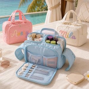 Puede incluir: Tres neceseres rectangulares en rosa, azul claro y crema. El bolso rosa lleva el nombre Avery y el crema el nombre Mila en bordado colorido. El neceser azul claro abierto muestra bolsillos de malla internos y ranuras para brochas.