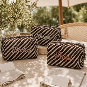 Op de afbeelding: Drie rechthoekige etuis met ritssluiting en een diagonaal gestreept patroon in donkerbruin en crème. Elk etui is geborduurd met een naam in cursief schrift: Brielle, Hadley en Paige. De tassen hebben een geweven textuur.