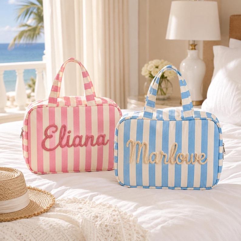 May include: Two rectangular fabric travel bags with top handles and vertical stripes. One bag is pink and white with the name Eliana embroidered in pink script. The other bag is blue and white with the name Marlowe embroidered in tan script.