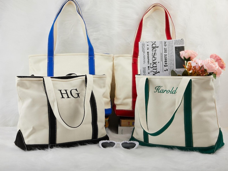 May include: Four cream canvas tote bags with coloured handles and trim. One bag has blue handles, another red, and a third green. The fourth bag has black trim and the initials "HG". One bag has the name "Harold" embroidered on it.