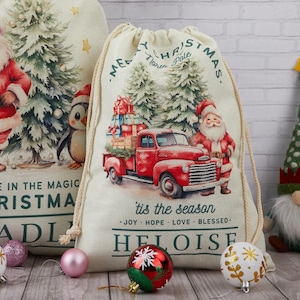 May include: Christmas drawstring bags featuring Santa Claus, a red truck laden with gifts, and Christmas trees. The bags display text saying "Believe in the Magic" and "'tis the season". Ornaments and a gnome are also visible.