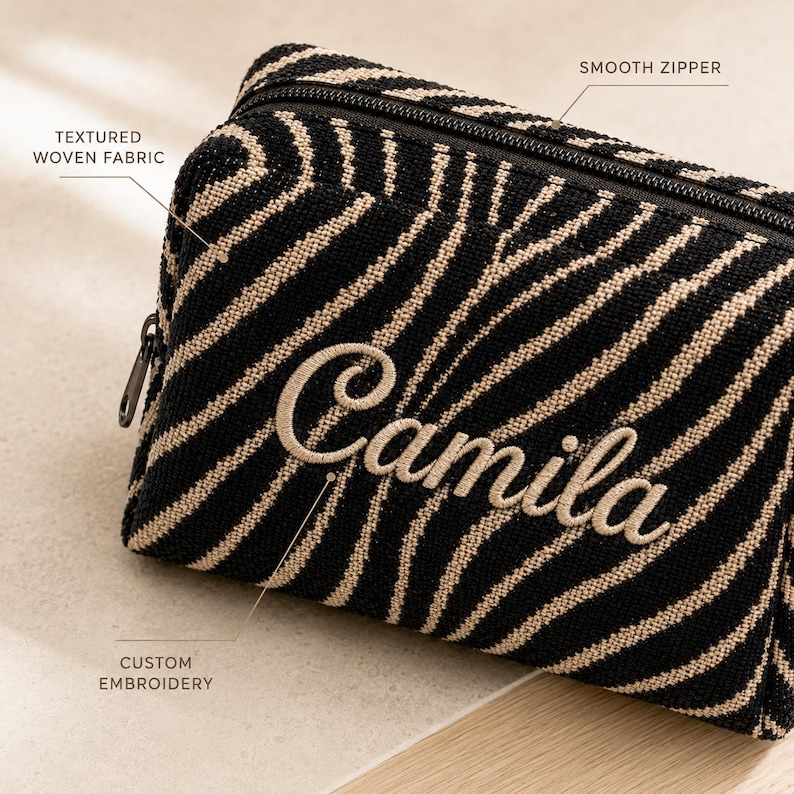 K&ouml;nnte beinhalten: Eine schwarz-beige Kosmetiktasche mit Zebramuster aus strukturiertem Webstoff, einem leichtg&auml;ngigen Rei&szlig;verschluss und dem Namen Camila in individueller Stickerei auf der Vorderseite. Das rechteckige Etui hat ein strukturiertes Design.