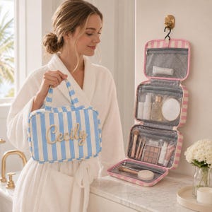 May include: A hanging toiletry bag with a blue and white vertical stripe pattern featuring the name Cecily in script lettering on the front. The bag unfolds into three clear zippered compartments containing various cosmetic items and brushes.