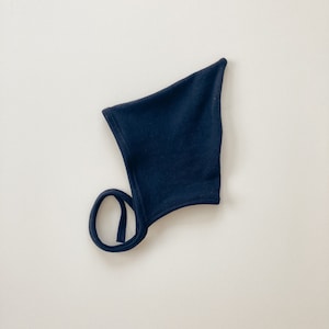 May include: A black baby bonnet with a tie. The bonnet is made of a soft, stretchy fabric.