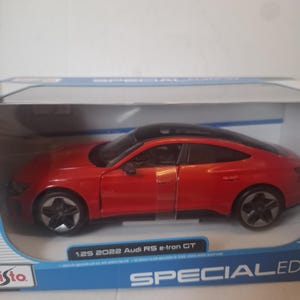 May include: A red 1:25 scale 2022 Audi RS e-tron GT model car with a black roof, presented in a blue and white box. The car features detailed wheels and is a special edition.