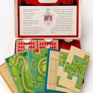 May include: An open box containing a golf-themed puzzle game. The box is red and white with text and a logo. Inside are puzzle cards with green golf course designs, a score card, and a solution card.