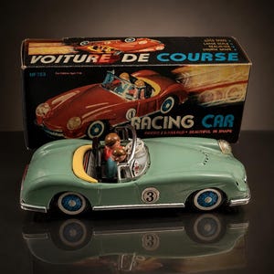 Könnte beinhalten: Ein grünes Vintage-Spielzeug-Rennwagen mit gelbem Akzent und der Nummer 3 an der Seite. Das Auto hat blau-weiße Räder und eine kleine Fahrerfigur. Auf der Schachtel hinter dem Auto steht "VOITURE DE COURSE" und "RACING CAR".