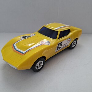 Peut inclure: Une voiture jouet jaune avec des roues noires et un pare-brise bleu. La voiture porte le numéro 45 sur le côté et le numéro 55 sur le capot. Elle présente des bandes de course et des logos de sponsors, dont "Champion" et "Esso".