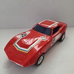 Pode incluir: Um carro de corrida de brinquedo vermelho com o número 45 no capô e na lateral. O carro tem uma faixa branca, azul e laranja no centro e a palavra "Champion" na lateral. O carro tem pneus pretos e um pára-brisas preto.