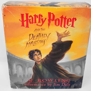 May include: A yellow, orange, and red book cover with the title "Harry Potter and the Deathly Hallows" in black text. The cover features an illustration of Harry Potter with his wand raised, looking up at the sky. The author, J.K. Rowling, and the performer, Jim Dale, are also listed on the cover.