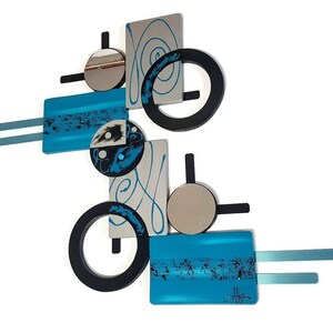May include: Abstract wall art sculpture with geometric shapes in black, silver, and turquoise blue. The sculpture features circles, squares, and swirls.