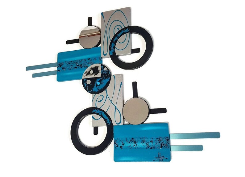 May include: Abstract wall art sculpture with geometric shapes in black, silver, and turquoise blue. The sculpture features circles, squares, and swirls.