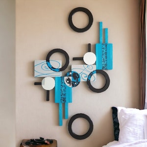 May include: Abstract wall art featuring a geometric design with black circles, white squares, and blue rectangles. The art is mounted on a white wall.