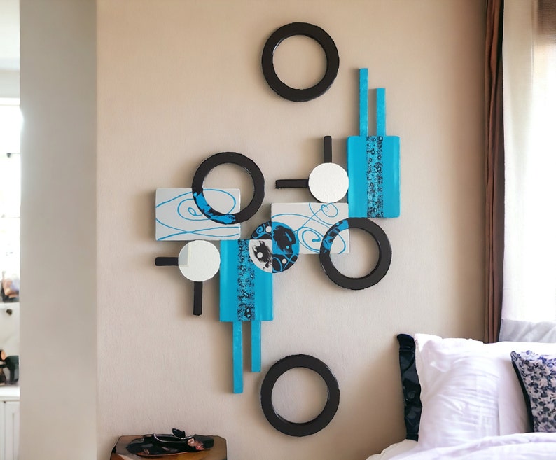 May include: Abstract wall art featuring a geometric design with black circles, white squares, and blue rectangles. The art is mounted on a white wall.