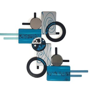 May include: Abstract wall art with geometric shapes in shades of blue, black, silver, and white. The piece features circles, squares, and rectangles with a swirling design.