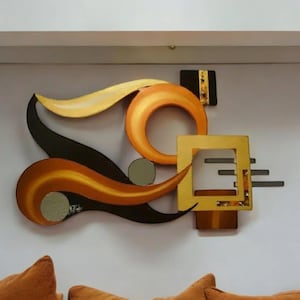 May include: Abstract wall art sculpture with a modern design. The sculpture features a combination of black, gold, and orange colors, with a geometric shape and flowing lines.