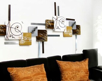 May include: A modern wall art piece featuring a geometric design with brown, white, and gray squares. The squares are arranged in a staggered pattern and are connected by thin metal rods. The art piece is mounted on a white wall above a black couch with orange throw pillows.