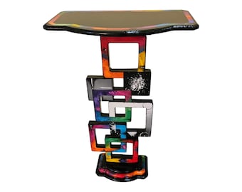May include: A colorful side table with a black top and a base made of stacked, painted squares. The squares are painted in various colors, including red, orange, yellow, green, blue, purple, and black.