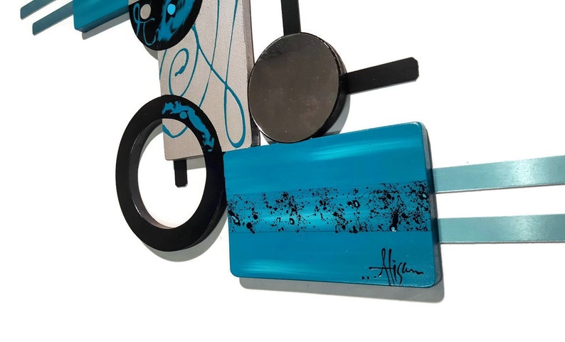 May include: Abstract wall art with geometric shapes in black, silver, and turquoise blue. The piece features a circle, a rectangle, and a square, with a mirrored circle in the center. The artist's signature is visible in the lower right corner.