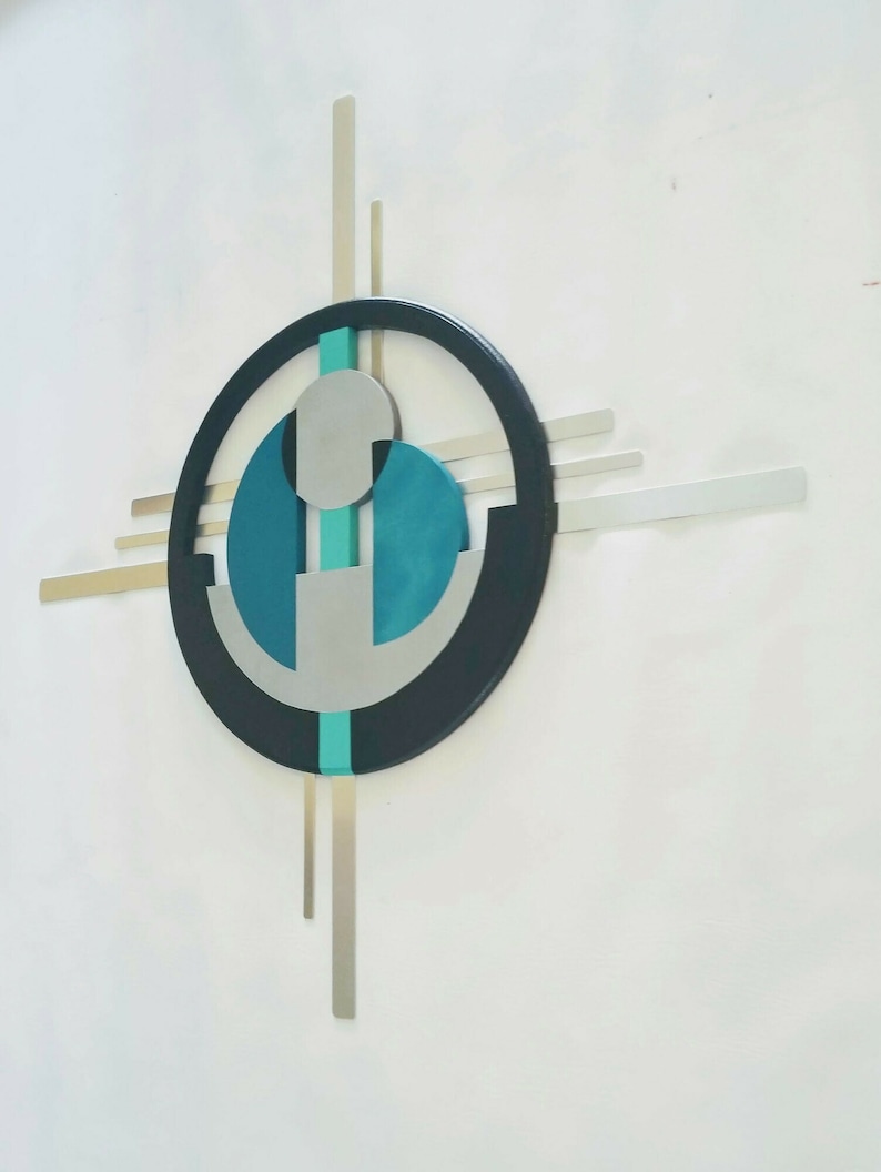 May include: A wall sculpture featuring a large black circular frame with intersecting horizontal and vertical silver metal bars. The center contains a teal vertical strip, two teal semi-circular shapes, and a light gray circular element.