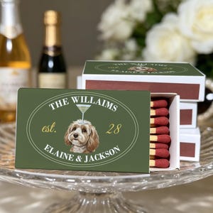 May include: A rectangular matchbox with a dark green cover featuring a white oval border, a brown and white dog illustration with a martini glass on its head, and the text THE WILLAIMS est. 28 ELAINE & JACKSON. The box contains wooden matches.